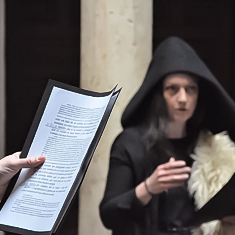Primer plano de mano sosteniendo un texto, segundo plano actriz interpretando en la actividad "Lecturas dramatizadas, Otoño 2021"